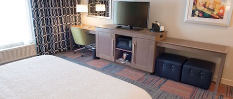 Habitación de hotel con cama, escritorio, televisor y espacios de almacenamiento.