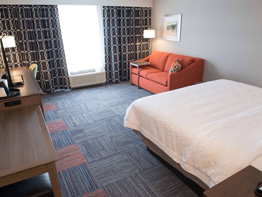 Hotelkamer met een bed, een bureau met een lamp, een bank en kamerbreed gordijn.
