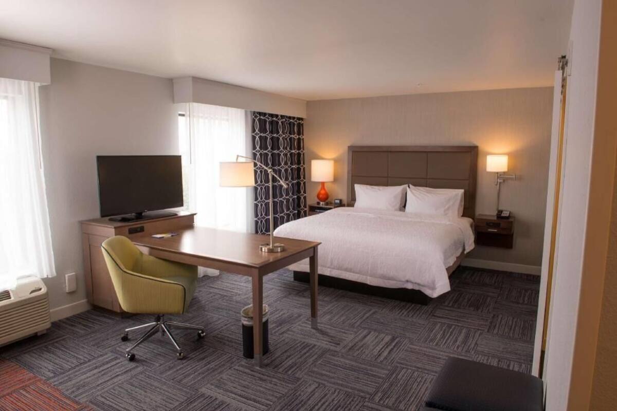 A hotel room with a bed, desk, chair, television, and lamps.