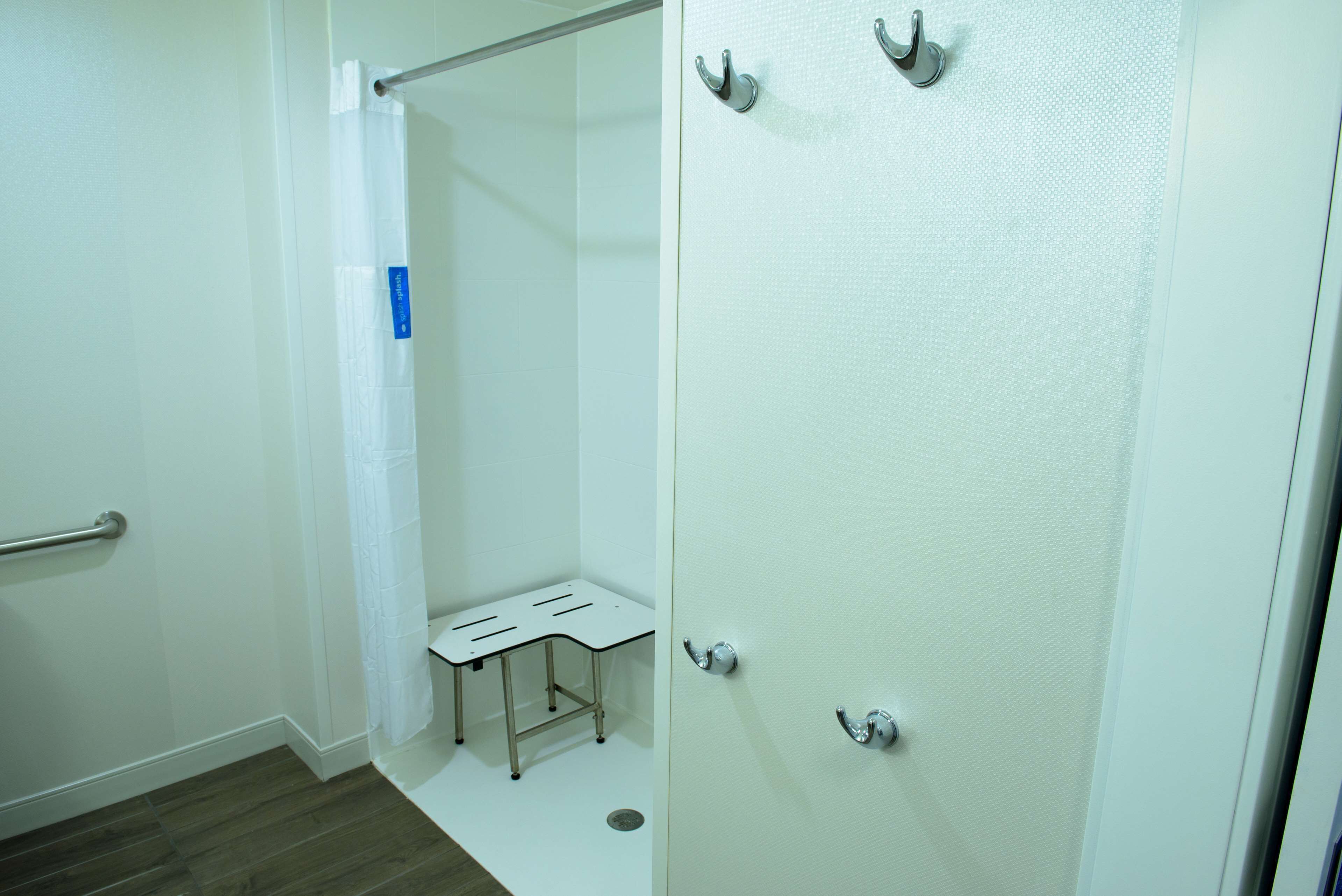 A bathroom with a shower, a small bench, and a toilet.