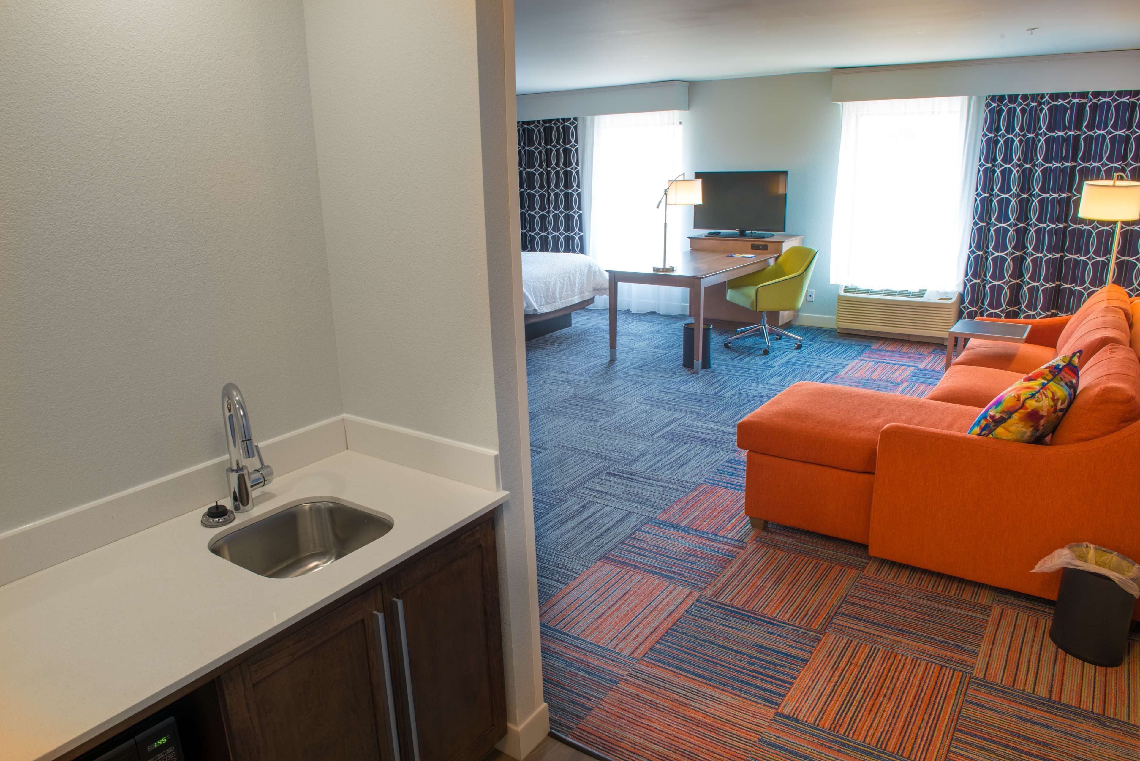 A hotel room with a kitchenette, a bed, a desk with a chair, a sofa, and a TV.