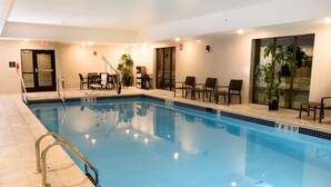 Un espace piscine d’hôtel comprenant une piscine à eau claire, une échelle en métal et plusieurs chaises longues.