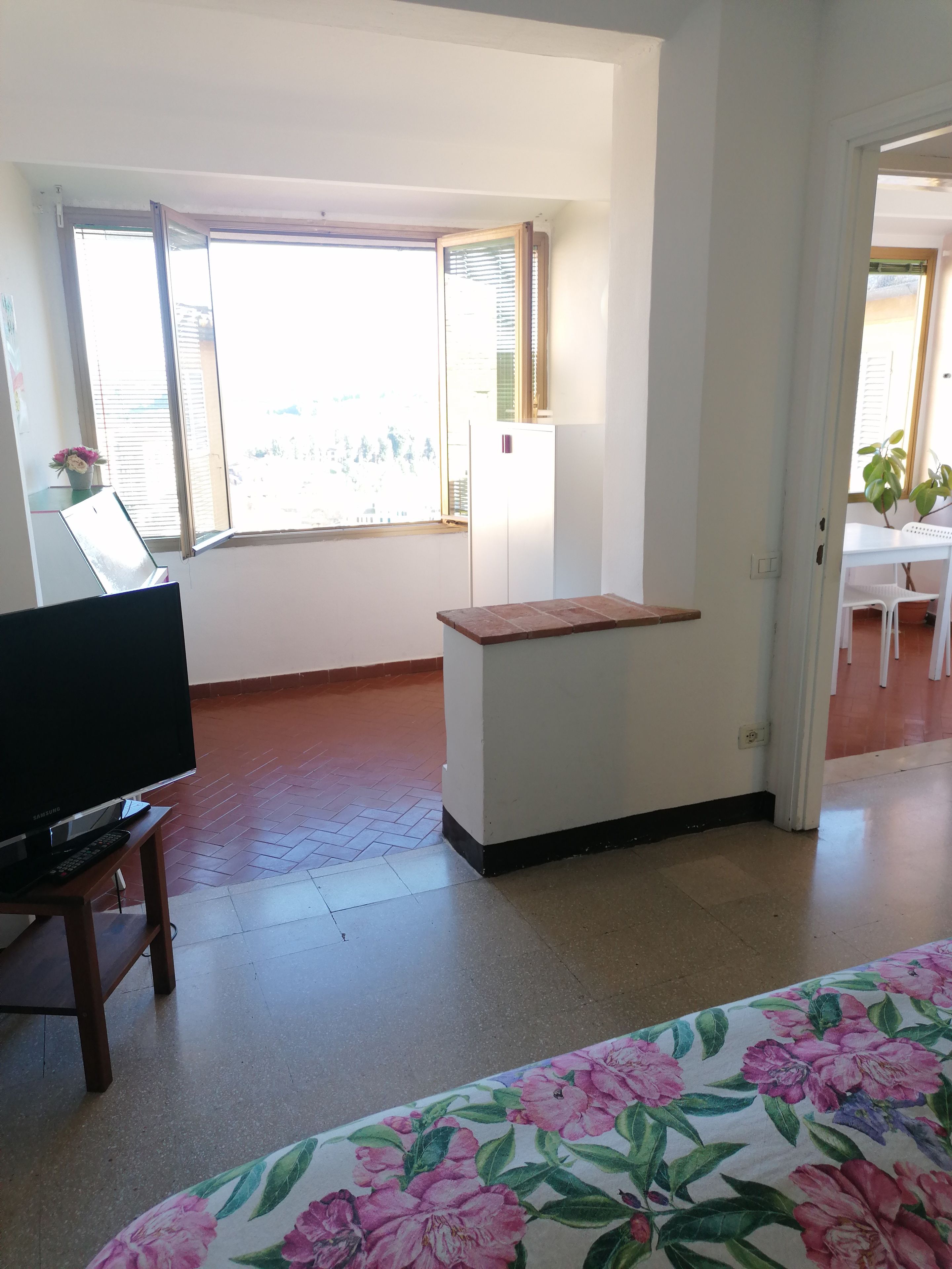 A room with a television on a stand, a small table, a window with blinds, and a door leading to another room.