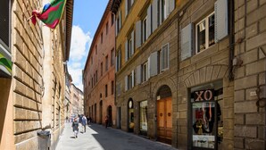 A narrow street lined with historic buildings, featuring a shop with a visible sign. - Casa di Osio (Siena)