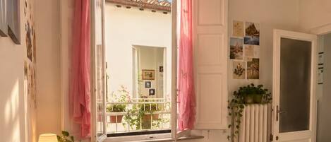 A bedroom with a bed, a window with curtains, a radiator, and a door.
