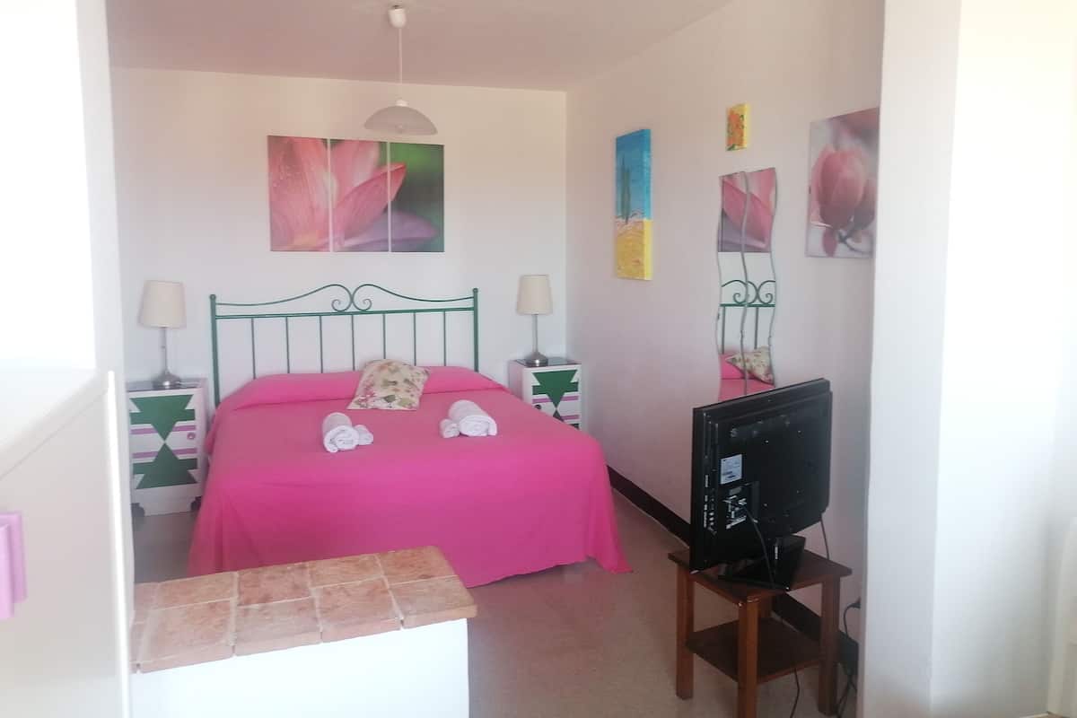 A bedroom with a bed, two bedside tables, a television, and artwork on the walls.
