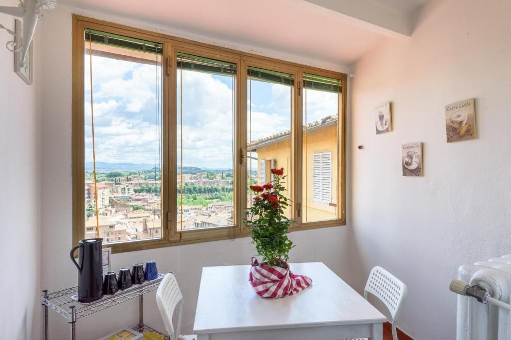 A room with a table, chairs, a radiator, and a window with a view of buildings.
