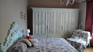 A bedroom with a large white wardrobe, a bed with patterned bedding, and a chair with a quilted cover. - Casa di Osio (Siena)