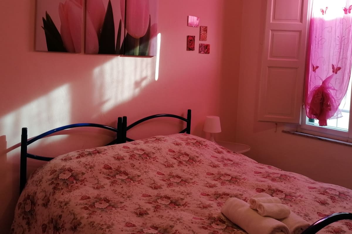 A bedroom with a bed, a nightstand, a window with curtains, and wall art.