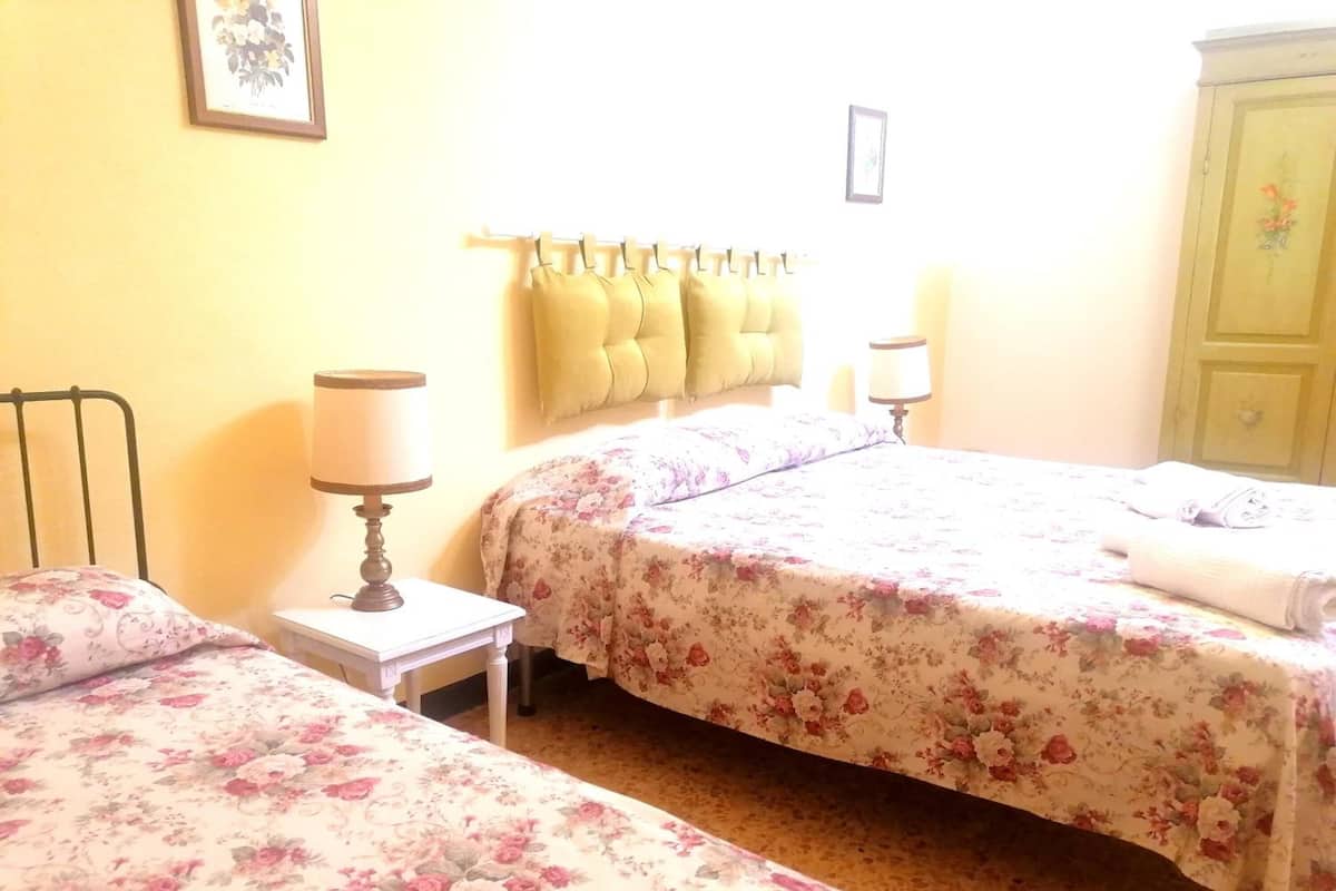 A bedroom with two single beds, a bedside table with a lamp, a wall-mounted shelf with towels, and a green wardrobe.
