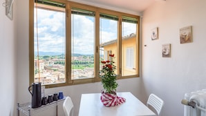 A balcony with a white table, a chair, a radiator, and a window with a view of buildings. - Casa di Osio (Siena)