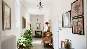 A hallway with a large teddy bear, potted plants, and framed artwork on the walls. - Casa di Osio (Siena)