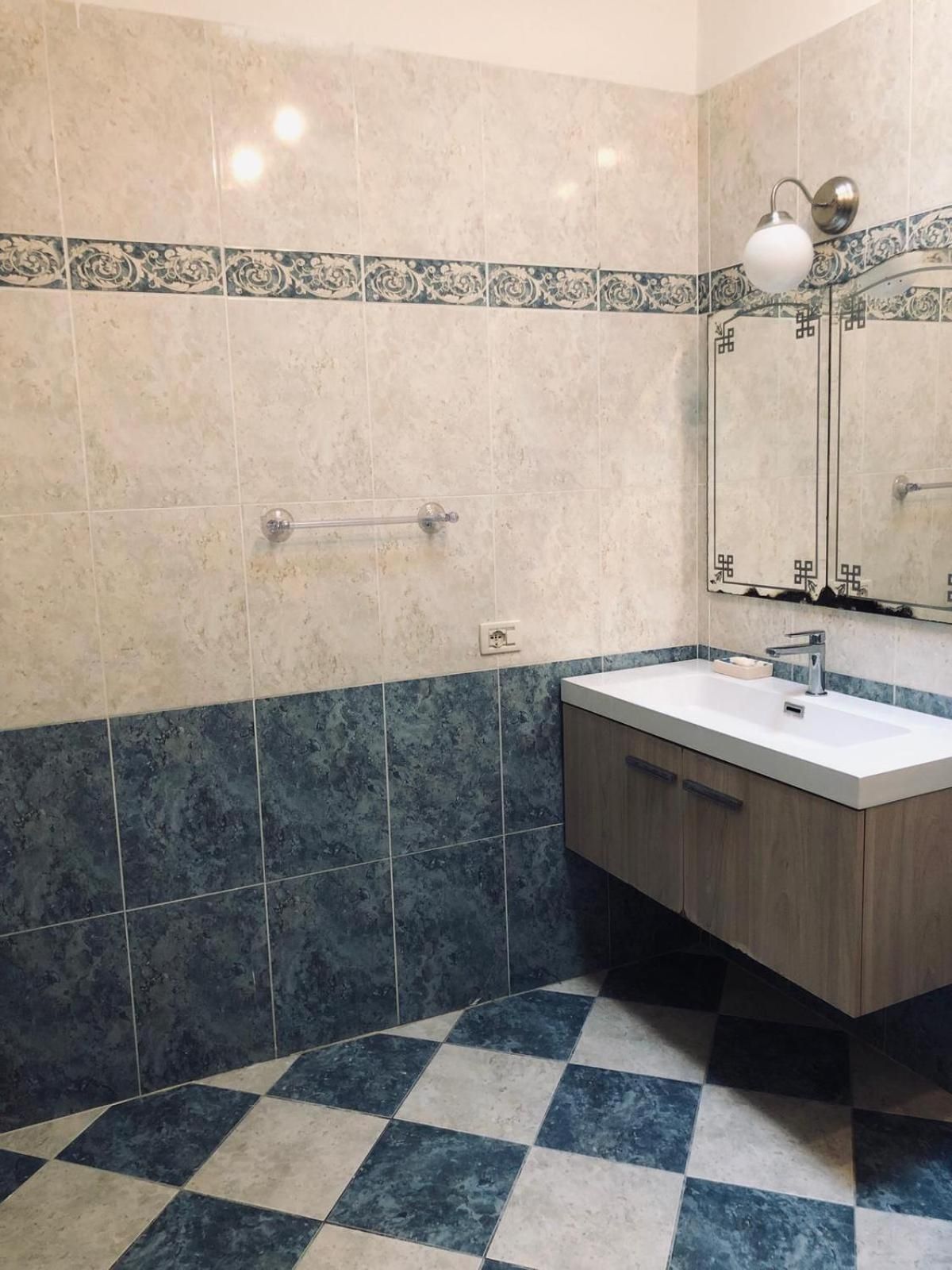 A bathroom with a checkered floor, a sink, and a mirror with a decorative tile border.