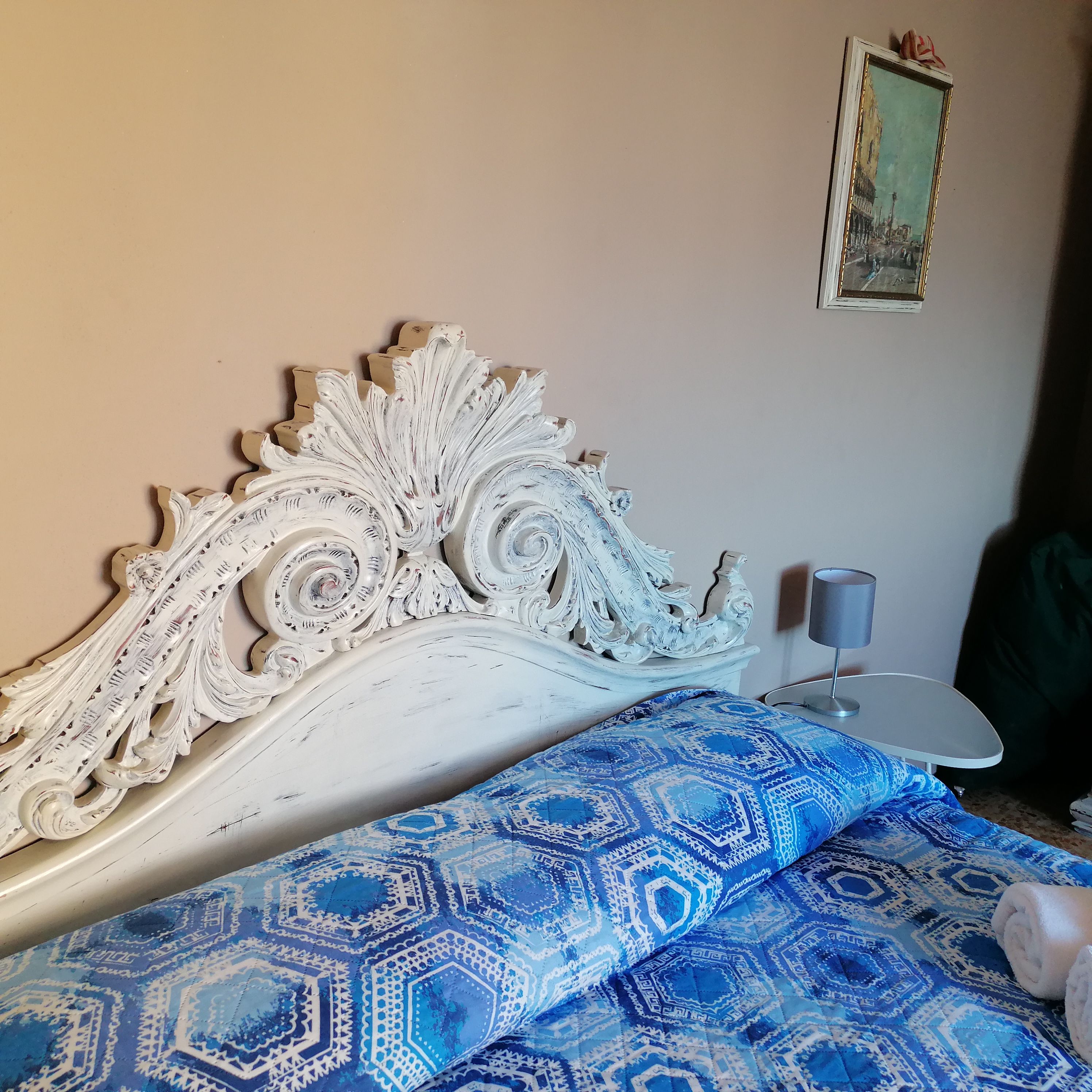 A bedroom with a decorative headboard, a patterned bedspread, a bedside table, and a framed picture on the wall.