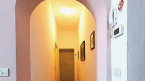 Un couloir étroit avec un plancher en bois, une porte au fond et un interphone fixé au mur.