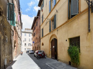 A narrow street with parked cars and buildings on either side.