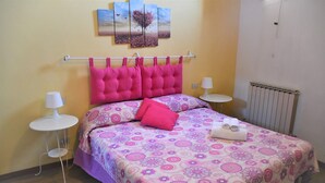Une chambre à coucher avec un lit, deux tables de chevet, un radiateur et un mur orné d’un tableau.