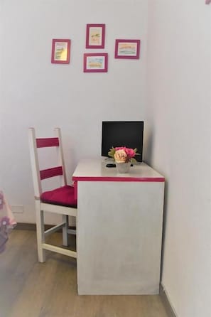 Een kleine kamer met een bureau, stoel en een wandplank met ingekaderde diploma’s.