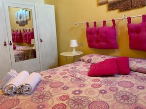 A room with a bed, a wardrobe, a small table with a lamp, and towels.