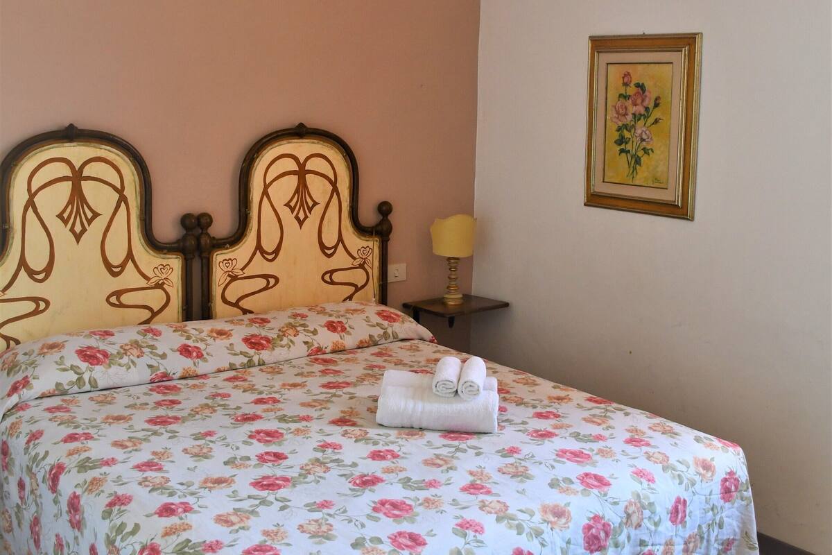 A bedroom with a floral bedspread, a wooden headboard, a bedside lamp, and a framed picture on the wall.