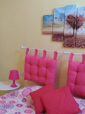 Een kamer met een bed, een nachtkastje, een lamp en een muur met drie schilderijen.