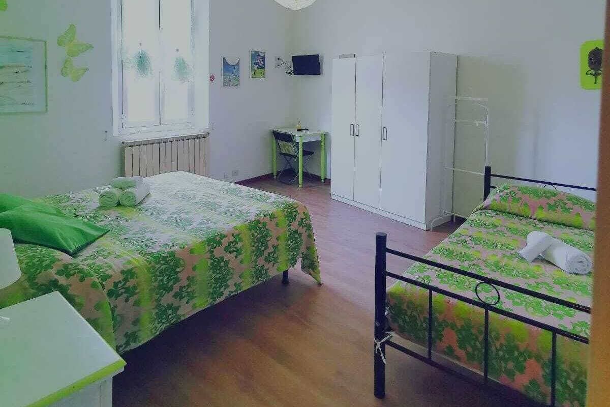 A room with two beds, a desk, a wardrobe, and a hanging light fixture.