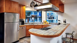 A modern kitchen with a stainless steel refrigerator, wooden cabinets, a large island with a tiled countertop, and a window overlooking a cityscape. - Seaport Village Inn Avalon (Avalon)