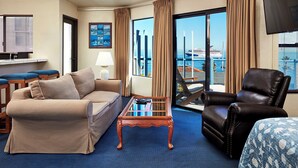 A hotel room with a sofa, armchair, and a small table. There is a large window with a view of the sea and a cruise ship. - Seaport Village Inn Avalon (Avalon)