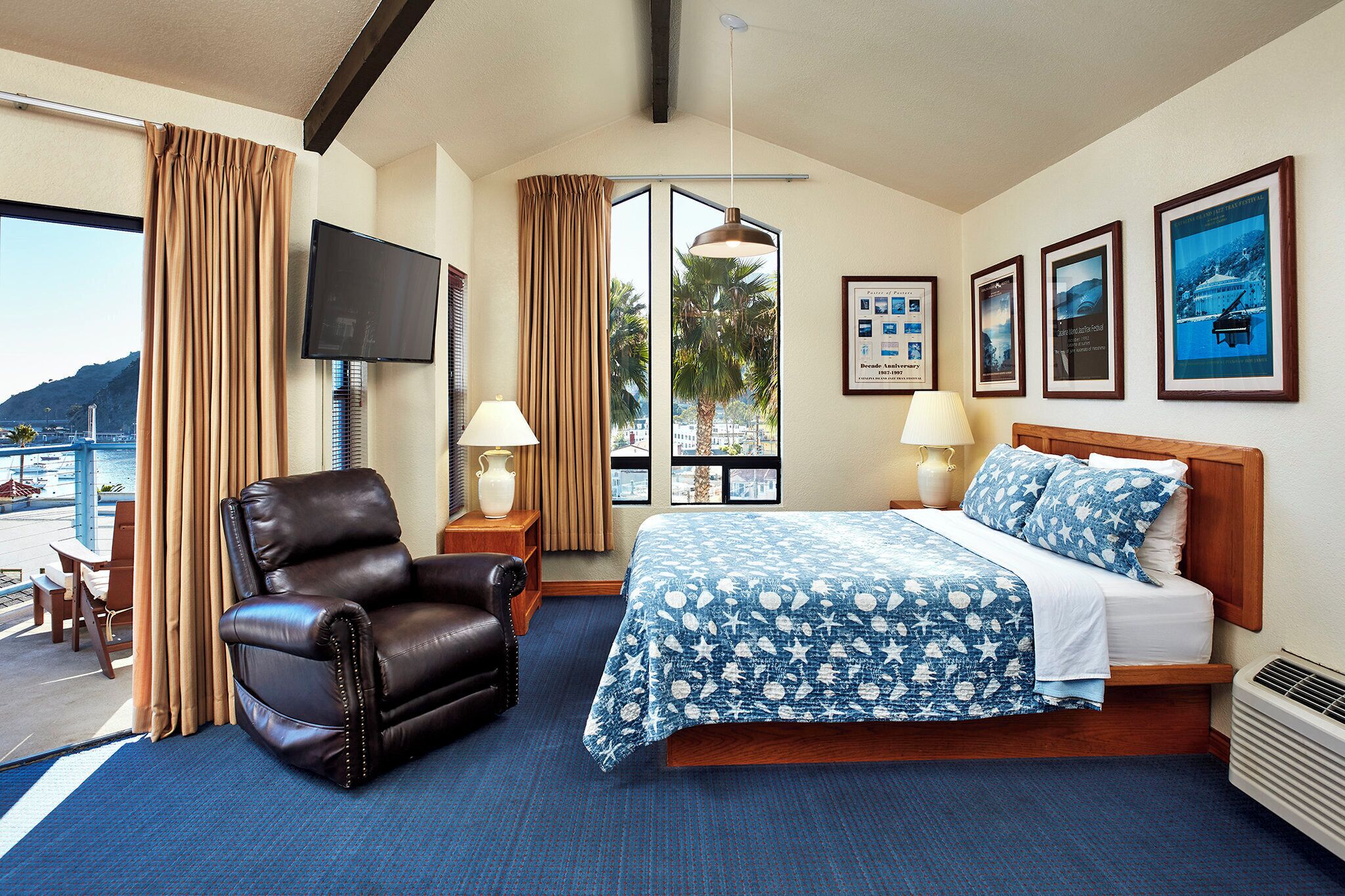 A hotel room with a bed, a leather chair, a TV, and framed pictures on the wall.