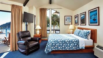 A hotel room with a bed, a leather chair, a TV, and framed pictures on the wall.