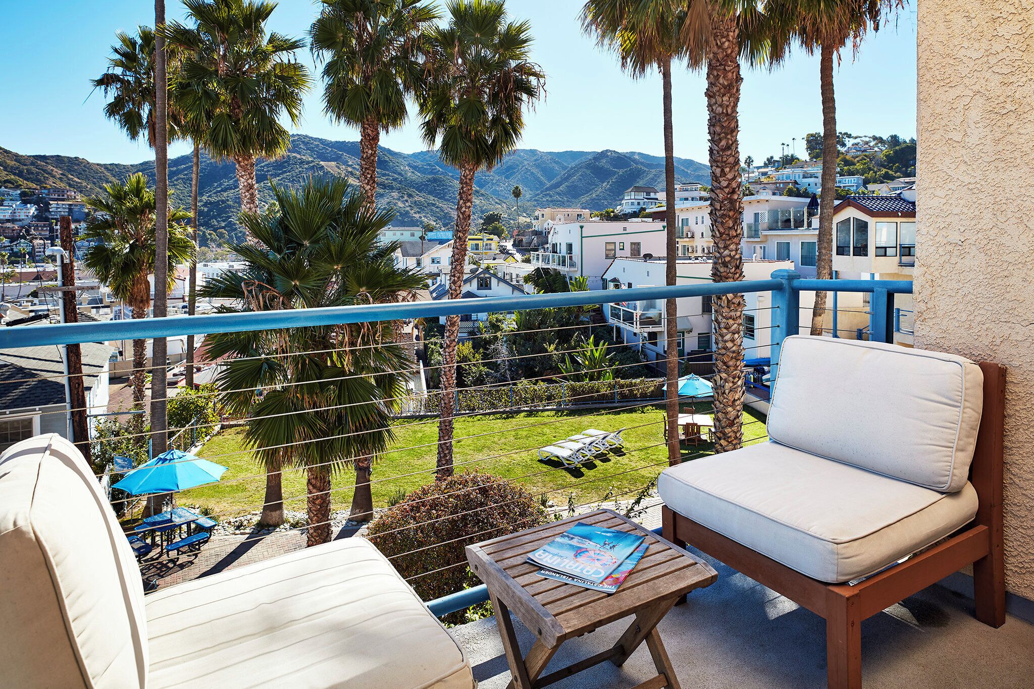 A balcony with a white sofa, a wooden table, and a blue umbrella.