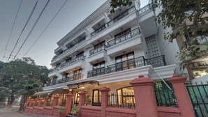 Un hotel de varios pisos con balcones, una entrada cubierta y un camino de acceso cerrado por una reja.