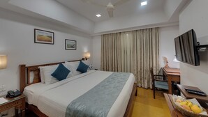 Habitación de hotel con cama, mesita de noche, lámpara, escritorio, silla, televisor y una cesta de frutas.