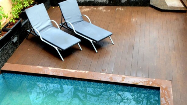 Piscina com duas espreguiçadeiras e um deck de madeira.