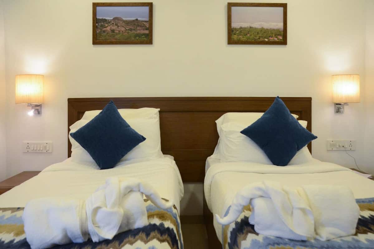A hotel room with two beds, each with a wooden headboard, white bedding, and blue pillows. There are wall-mounted lamps on either side of the beds.
