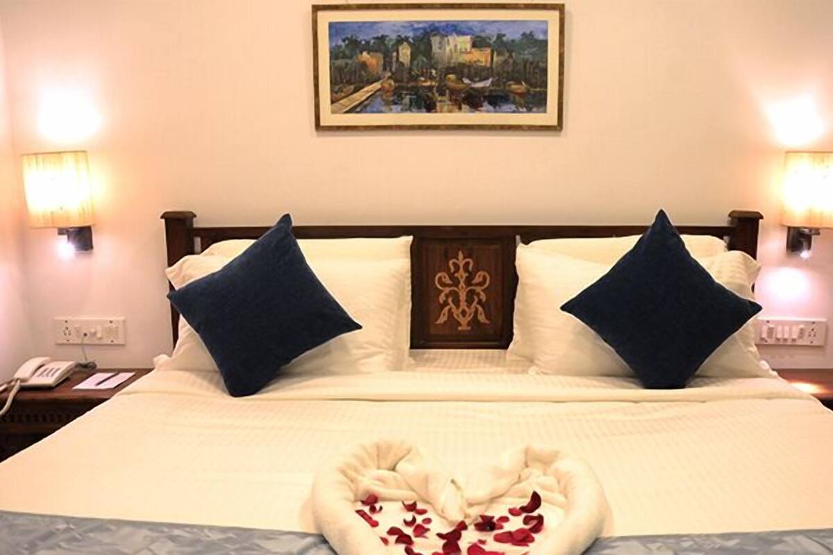 A hotel room with a neatly made bed, two bedside lamps, a painting on the wall, and a telephone on the nightstand.