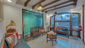 Una habitación con un ventanal grande, una pared verde con textura, un banco de madera, una mesa con un tocadiscos y un ventilador de techo.