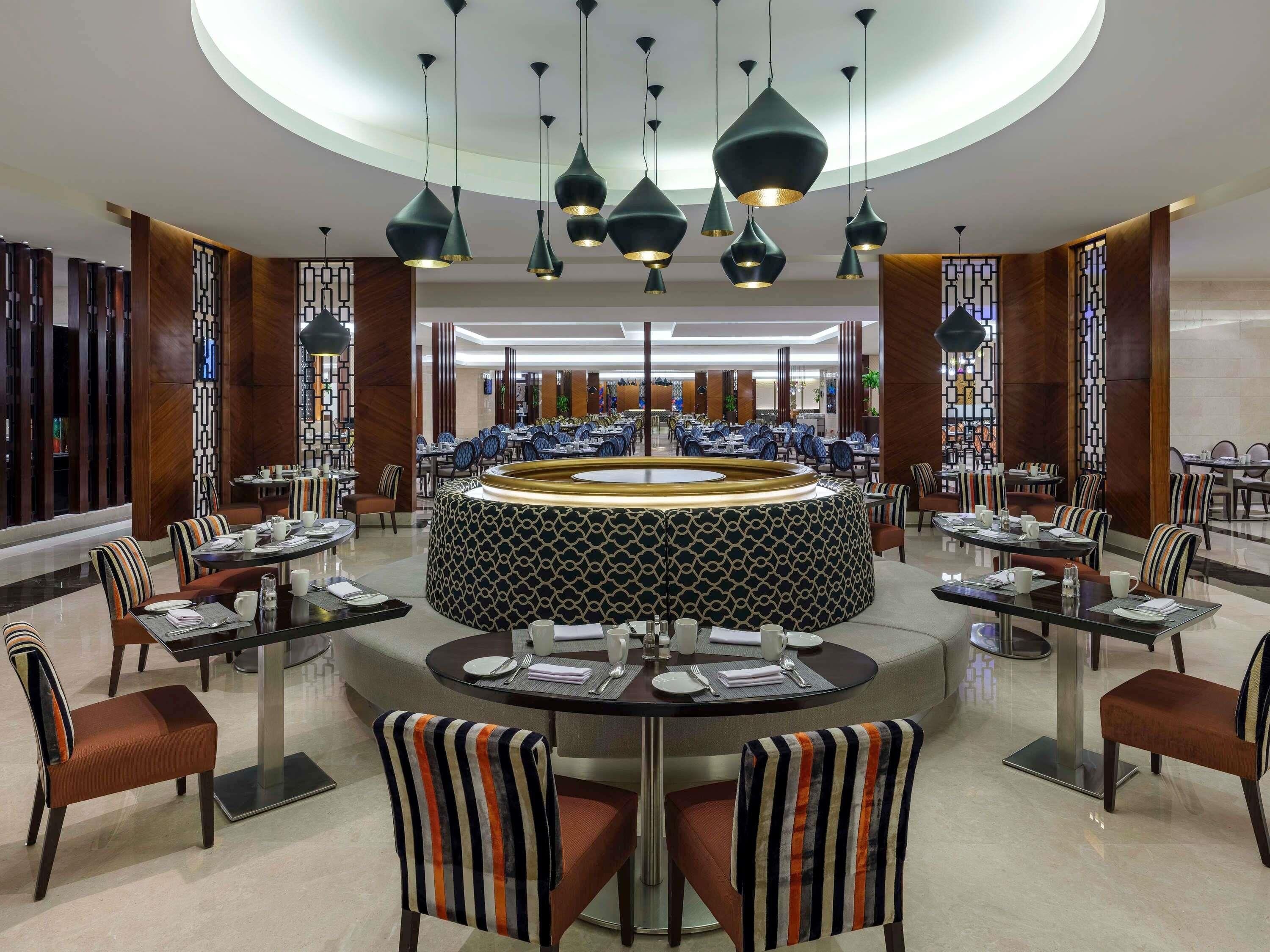 A modern restaurant with round tables, striped chairs, and pendant lighting.