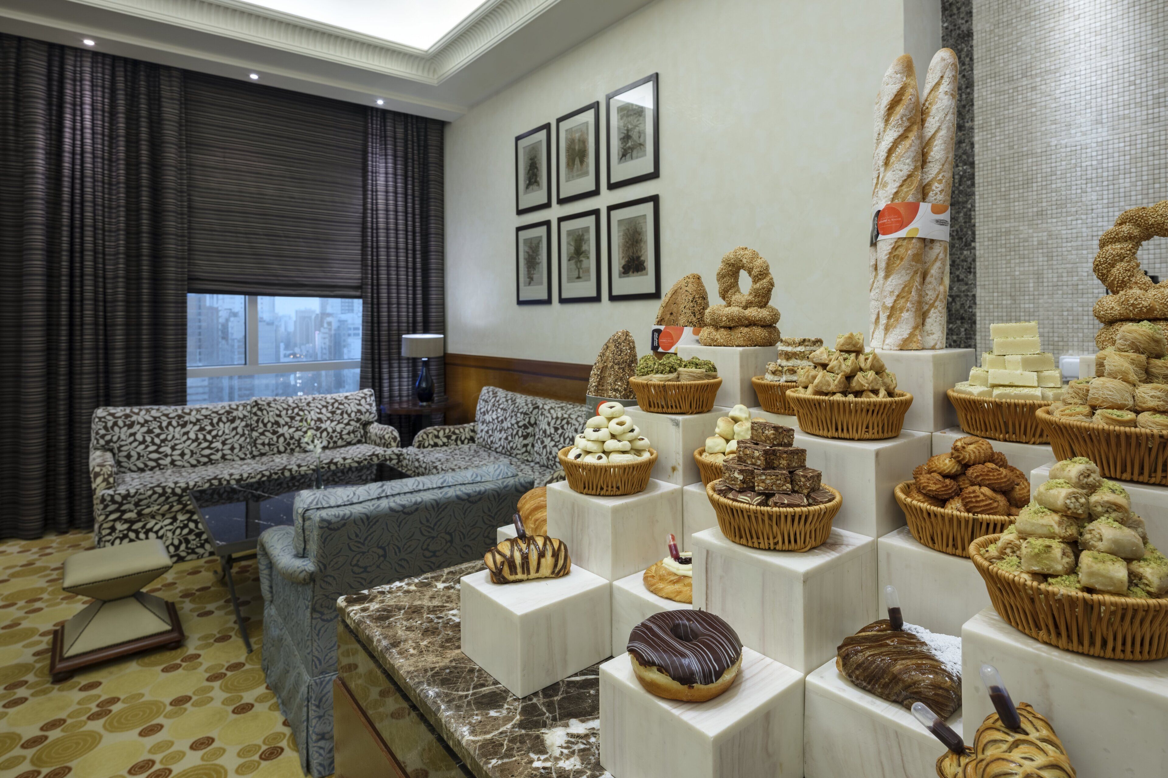 A hotel lobby with a seating area, a display of pastries, and framed pictures on the wall.