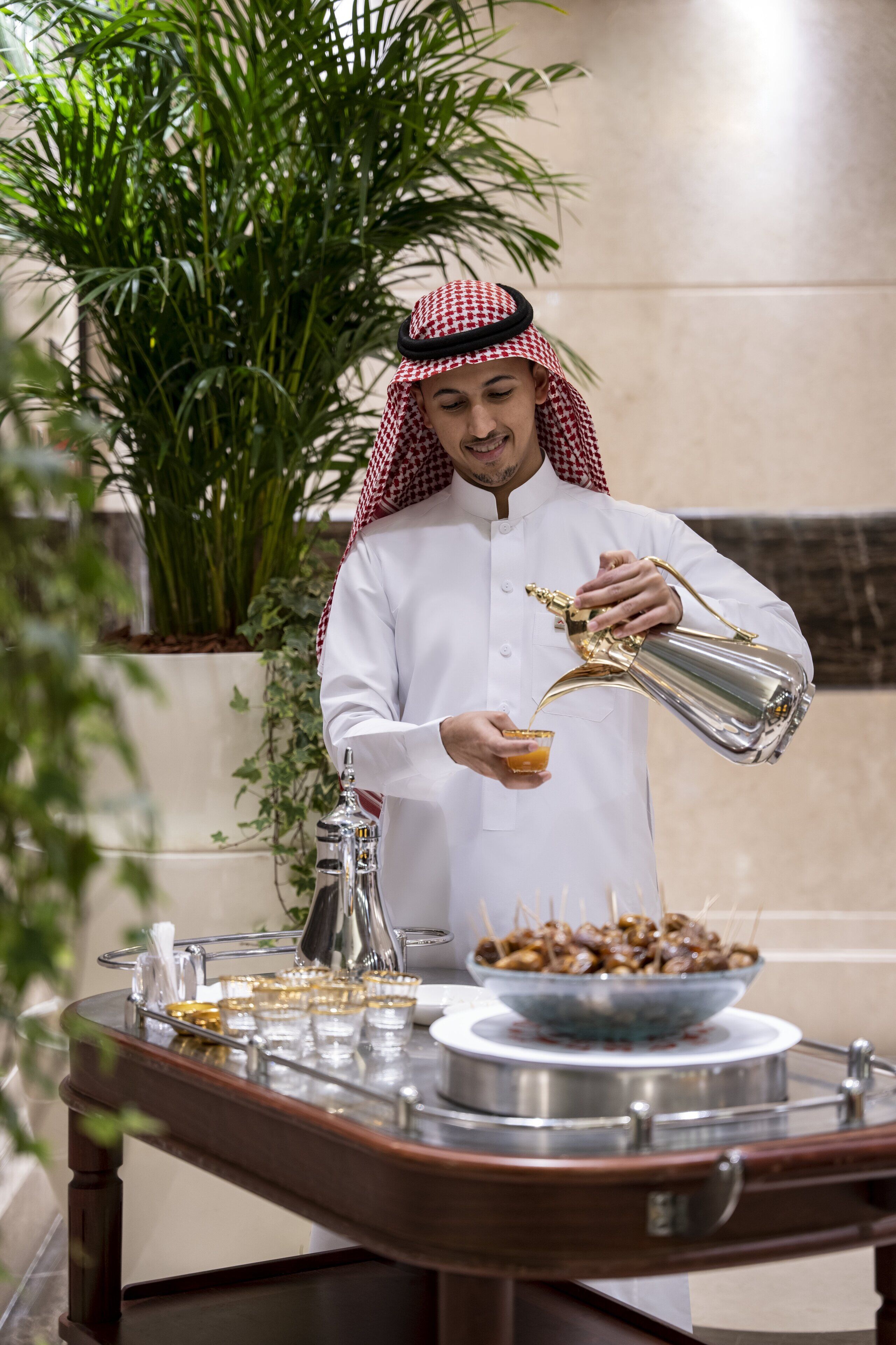 A person pouring a drink from a golden pitcher into a glass.