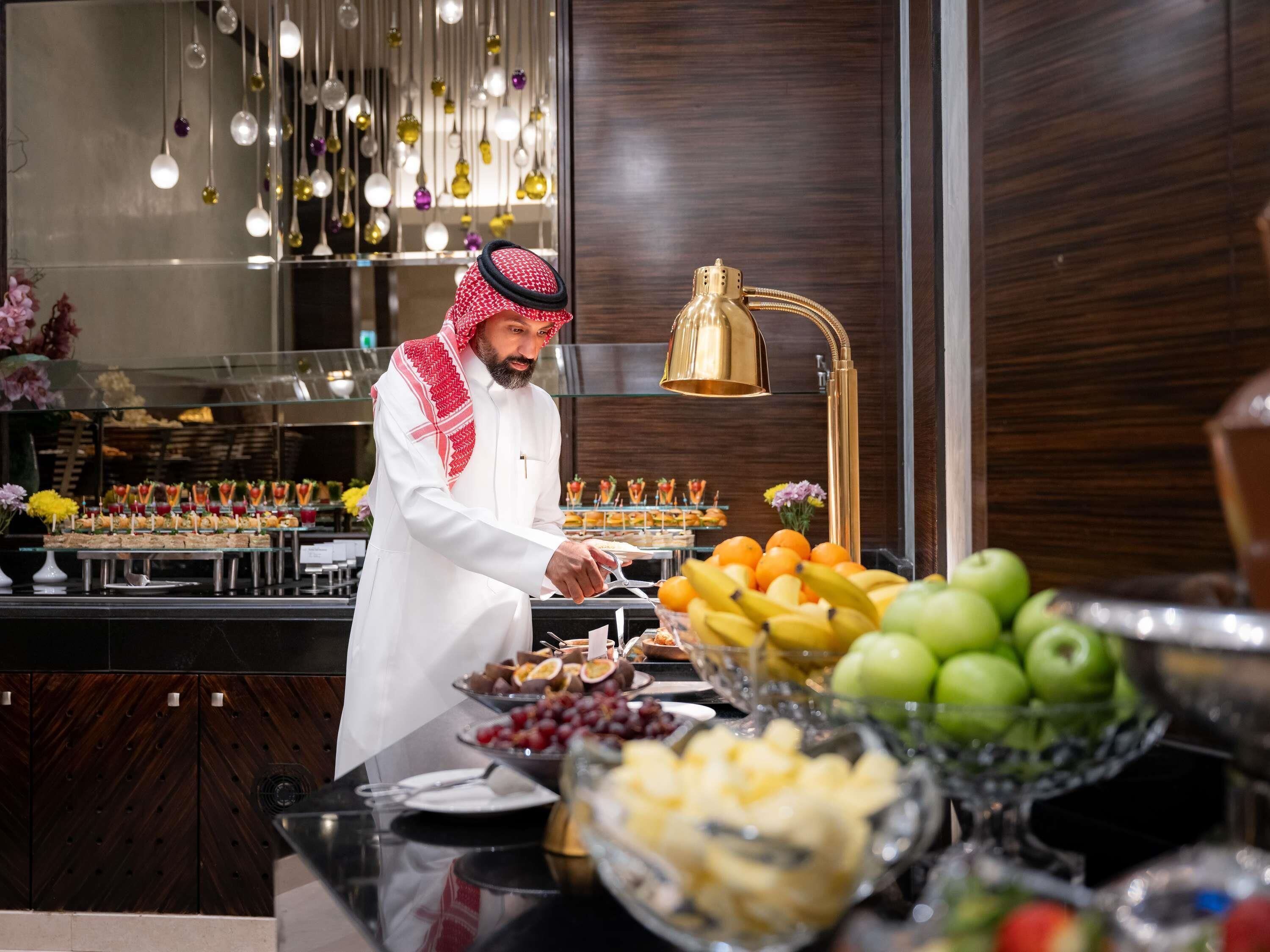 A buffet setup with various food items, a person serving, and a modern interior with hanging lights.
