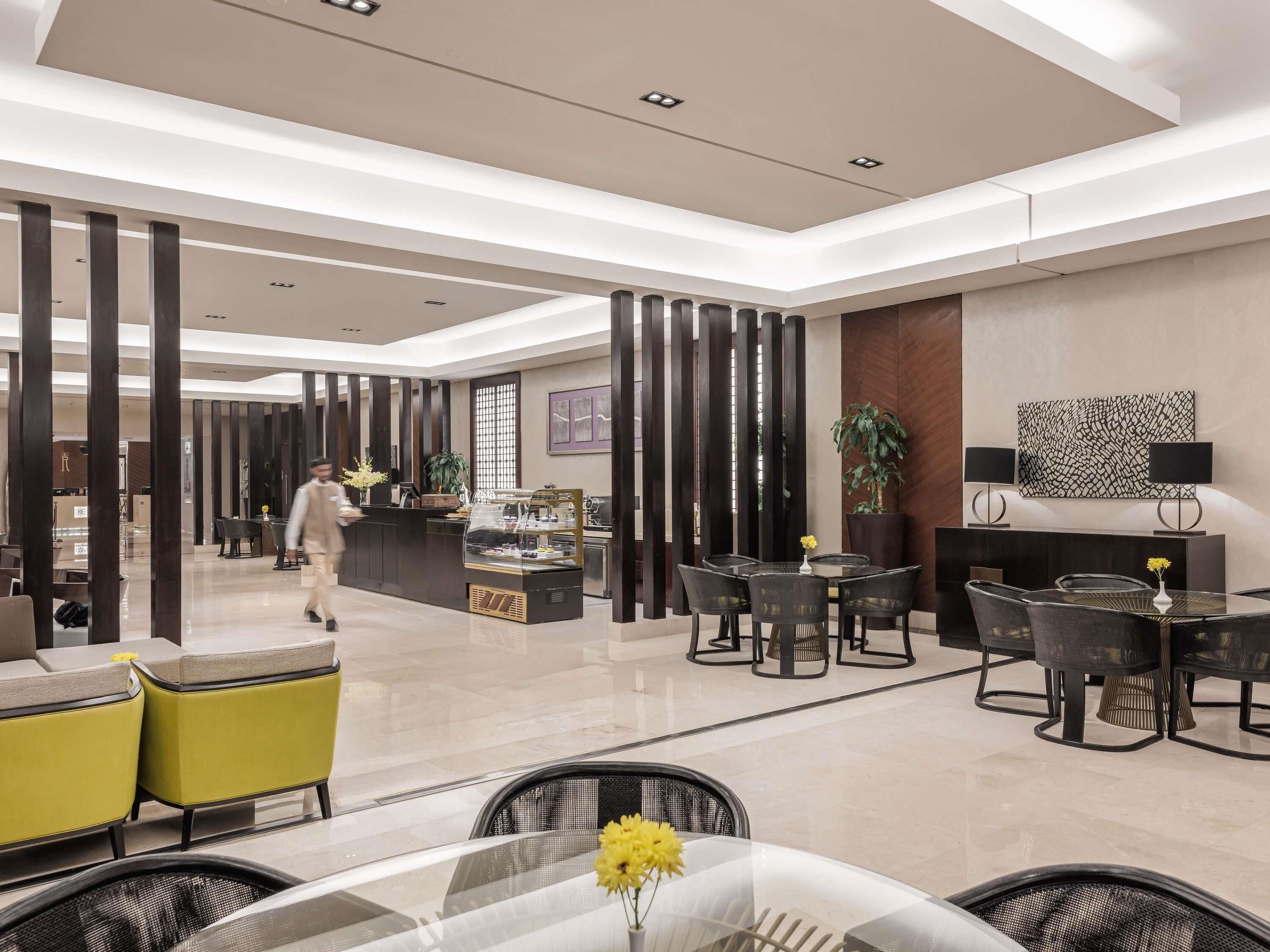A modern hotel lobby with a reception desk, seating area, and a dining space.