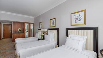 Une chambre d’hôtel avec trois lits, un bureau, une chaise et un miroir.