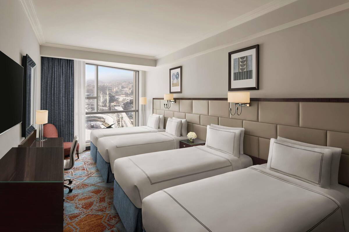 Une chambre d’hôtel avec une grande fenêtre, deux lits, un bureau et une chaise.