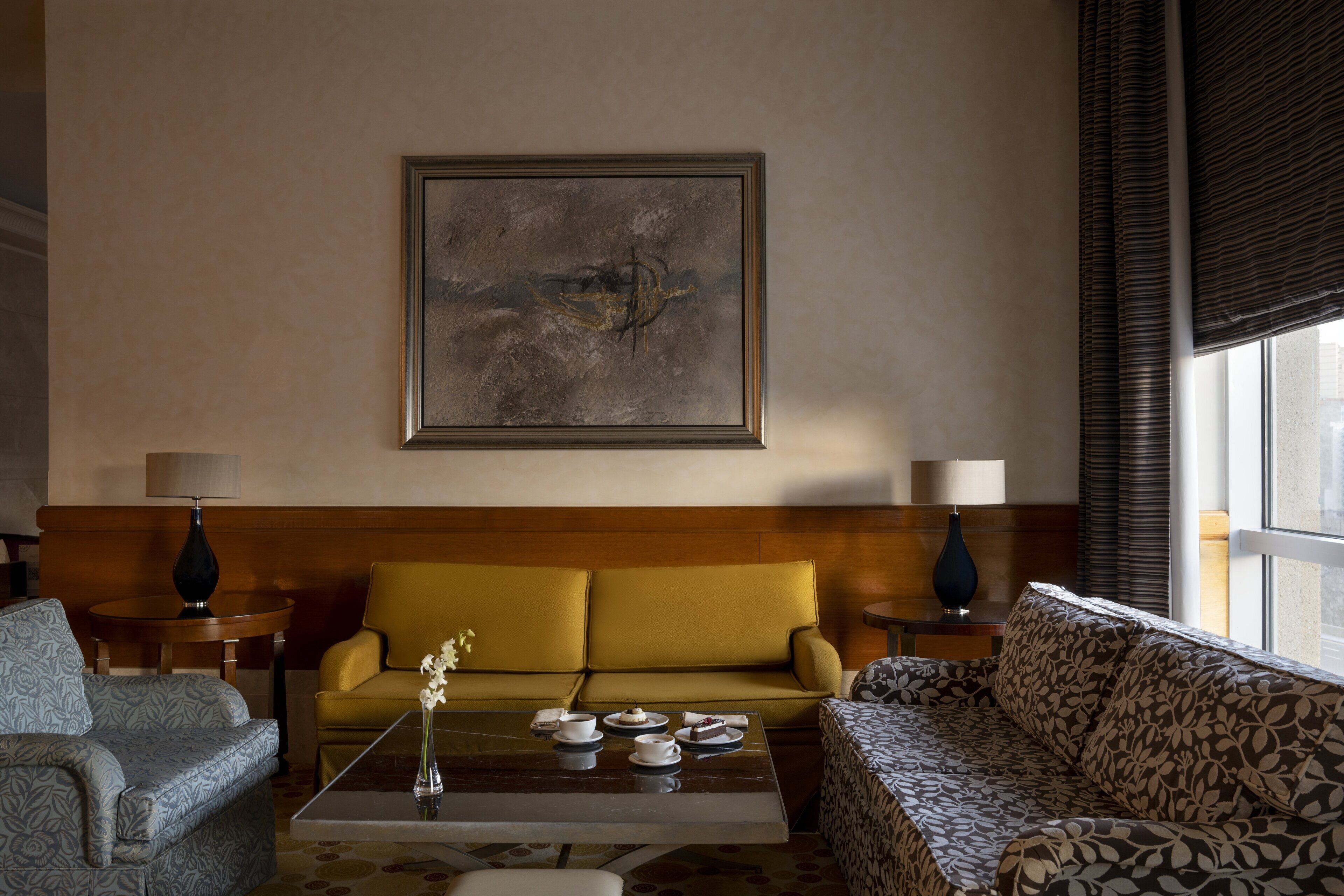 A modern living room with a sofa, armchairs, a coffee table, and a painting on the wall.