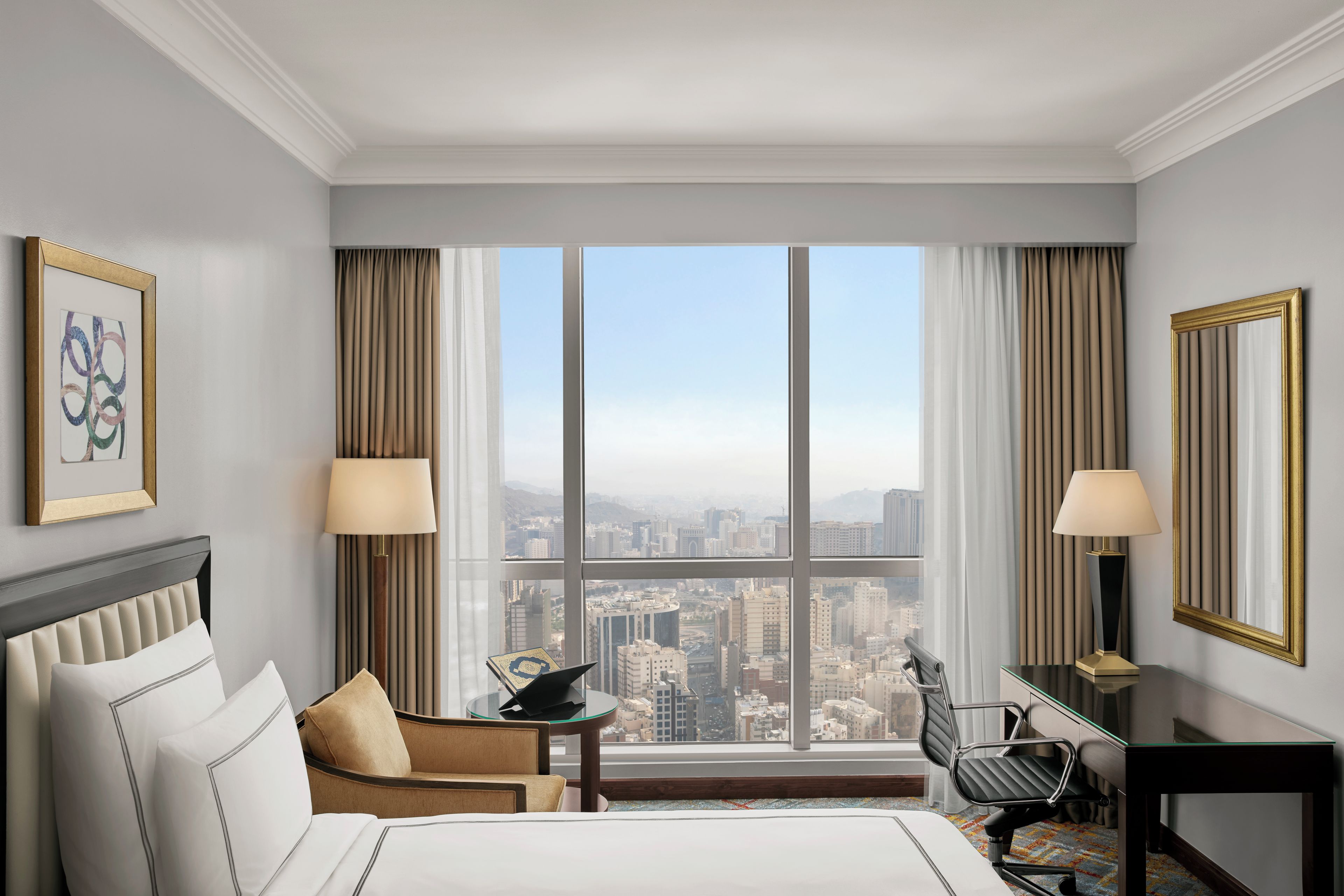 Ein Hotelzimmer mit großem Fenster, einem Bett, einem Schreibtisch und einem Sessel.