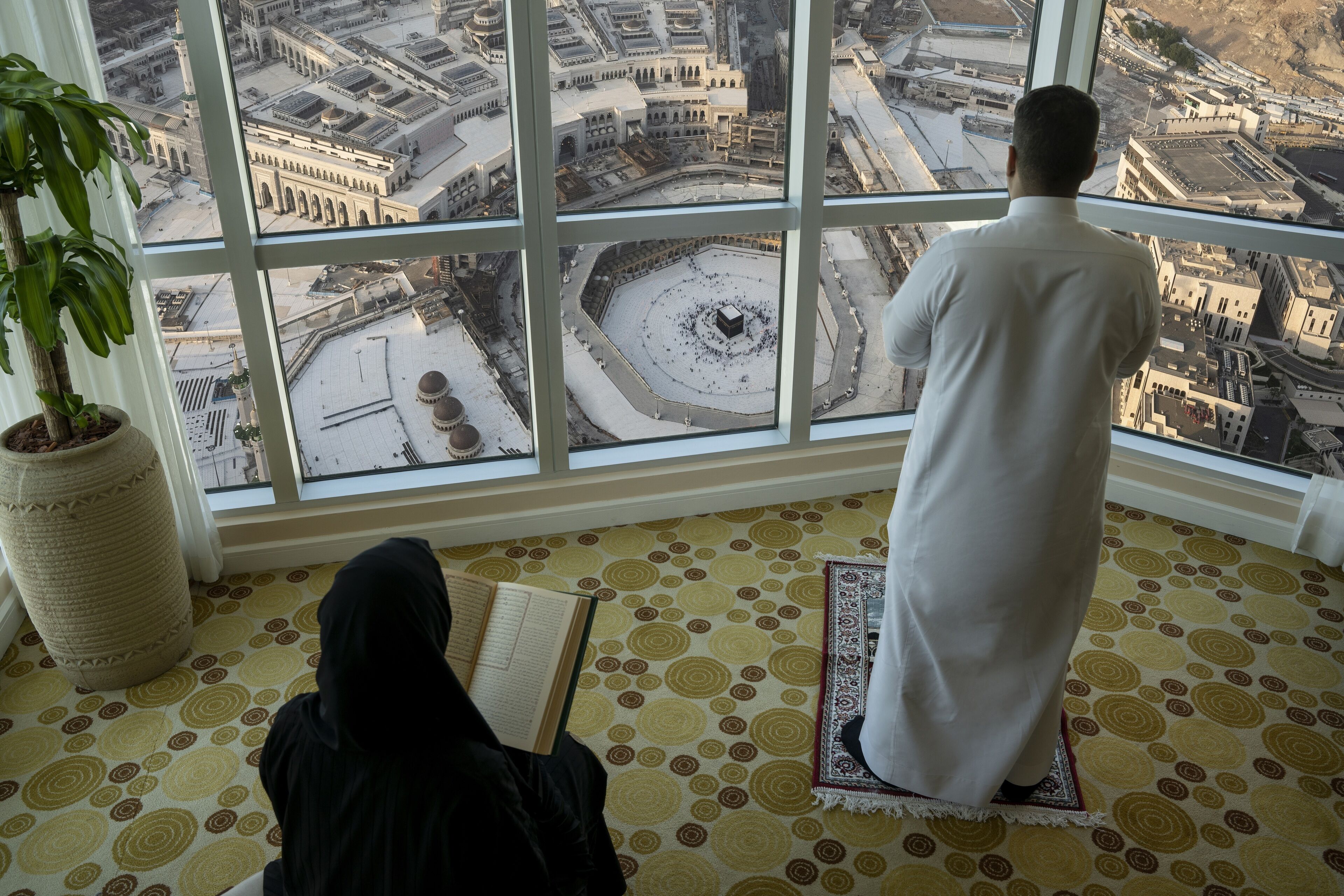 A person praying in a room with a large window overlooking a mosque.
