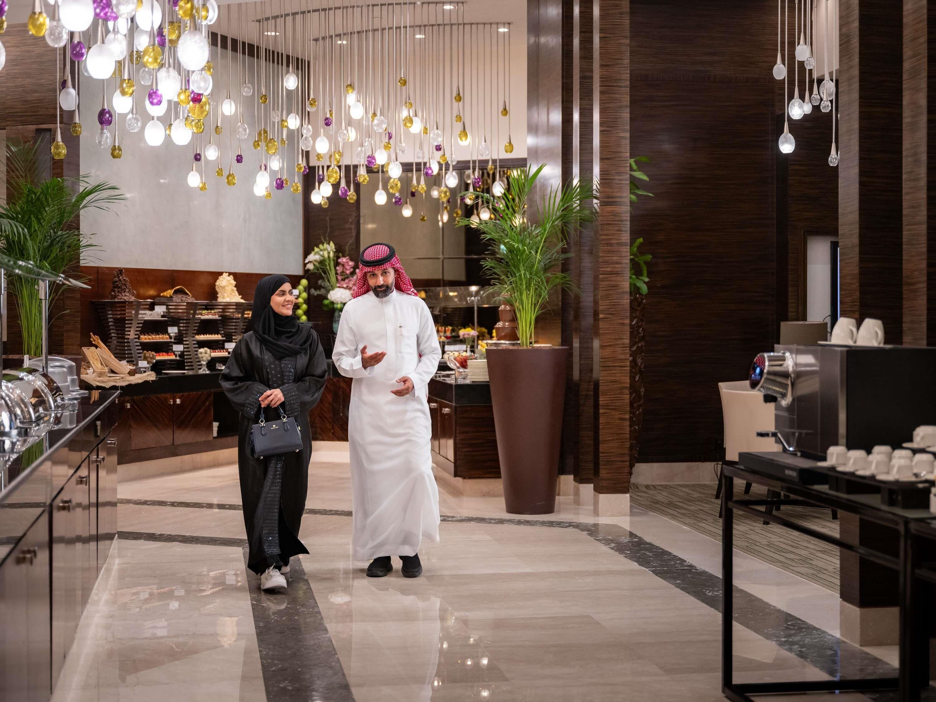 A modern hotel lobby with a marble floor, a reception desk, and a coffee machine.