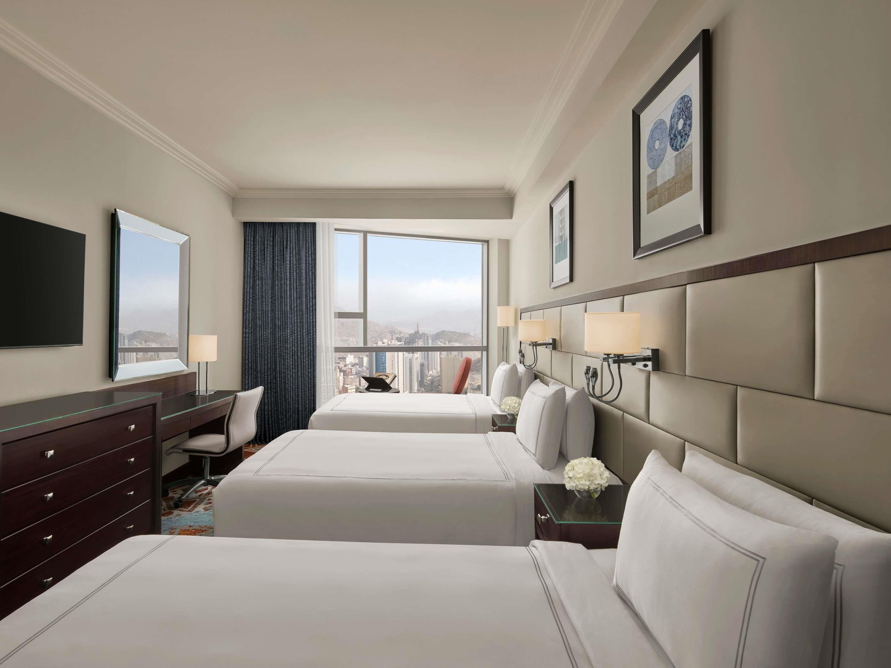 Habitación de hotel con dos camas, un escritorio, una cómoda y un ventanal con vistas a la ciudad.