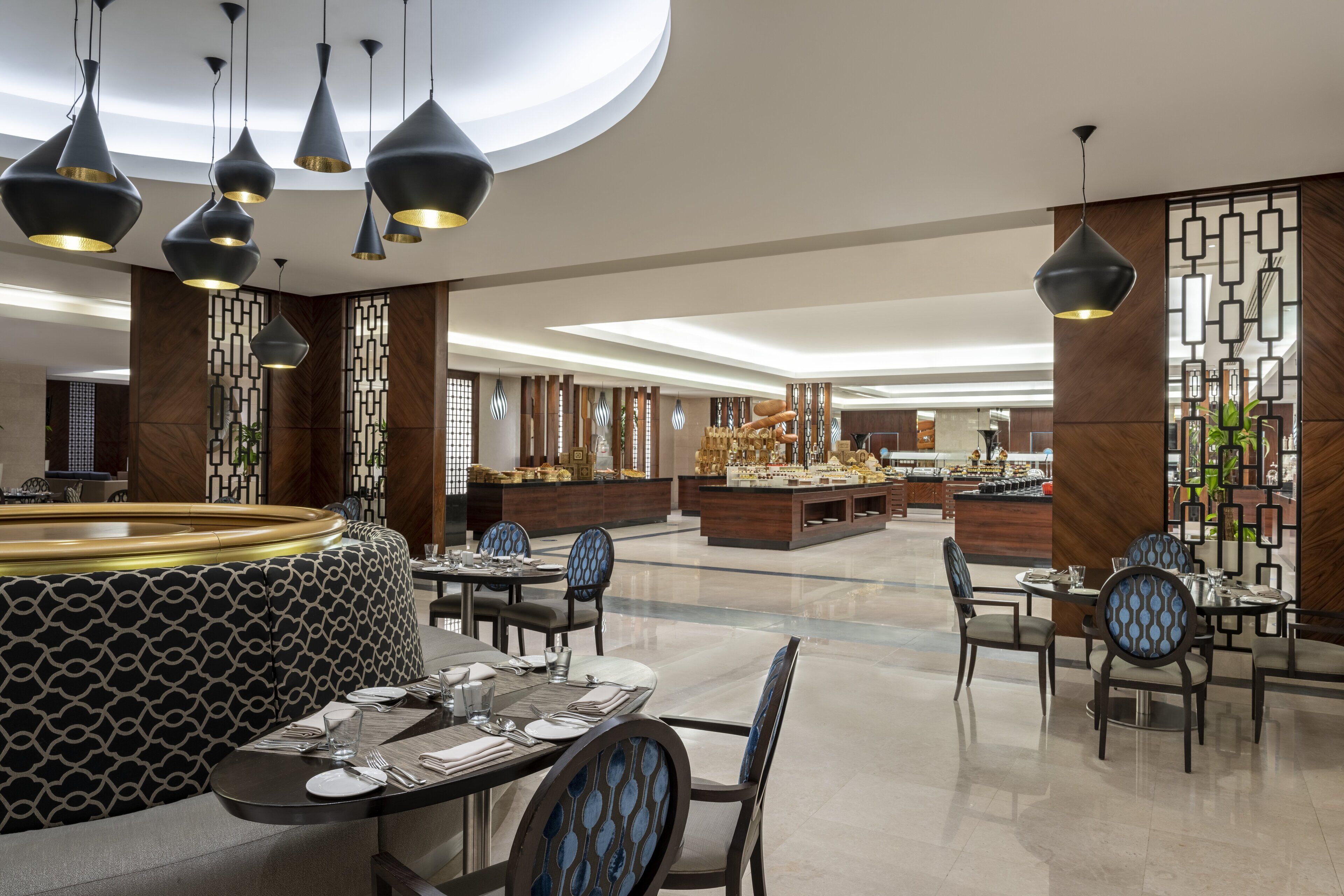 Un moderno vestíbulo de hotel con mesas redondas, asientos con estampado blanco y negro e iluminación colgante contemporánea.